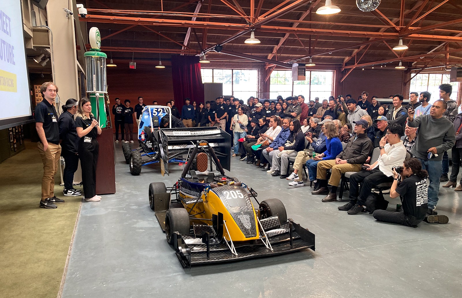 A student formula car unveiled before a seated audience in the hall
